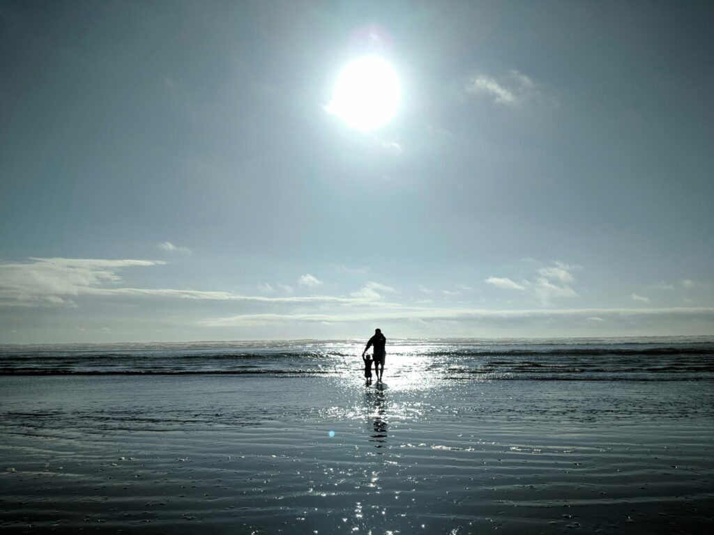 parent walks with their child on the beach on a sunny day