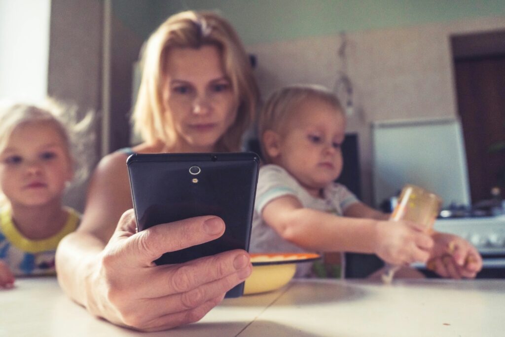 a mom looks at her phone while her two young children sit on either side of her